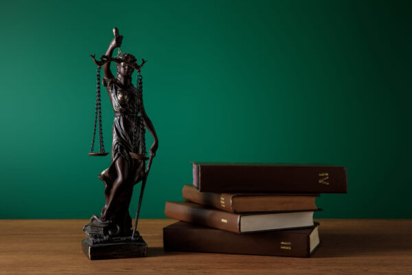 bronze statuette with scales of justice and volumes of books on wooden table on dark green
