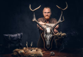 Taxidermist standing near a table with handmade trophy, owl scarecrow, and the fox skin